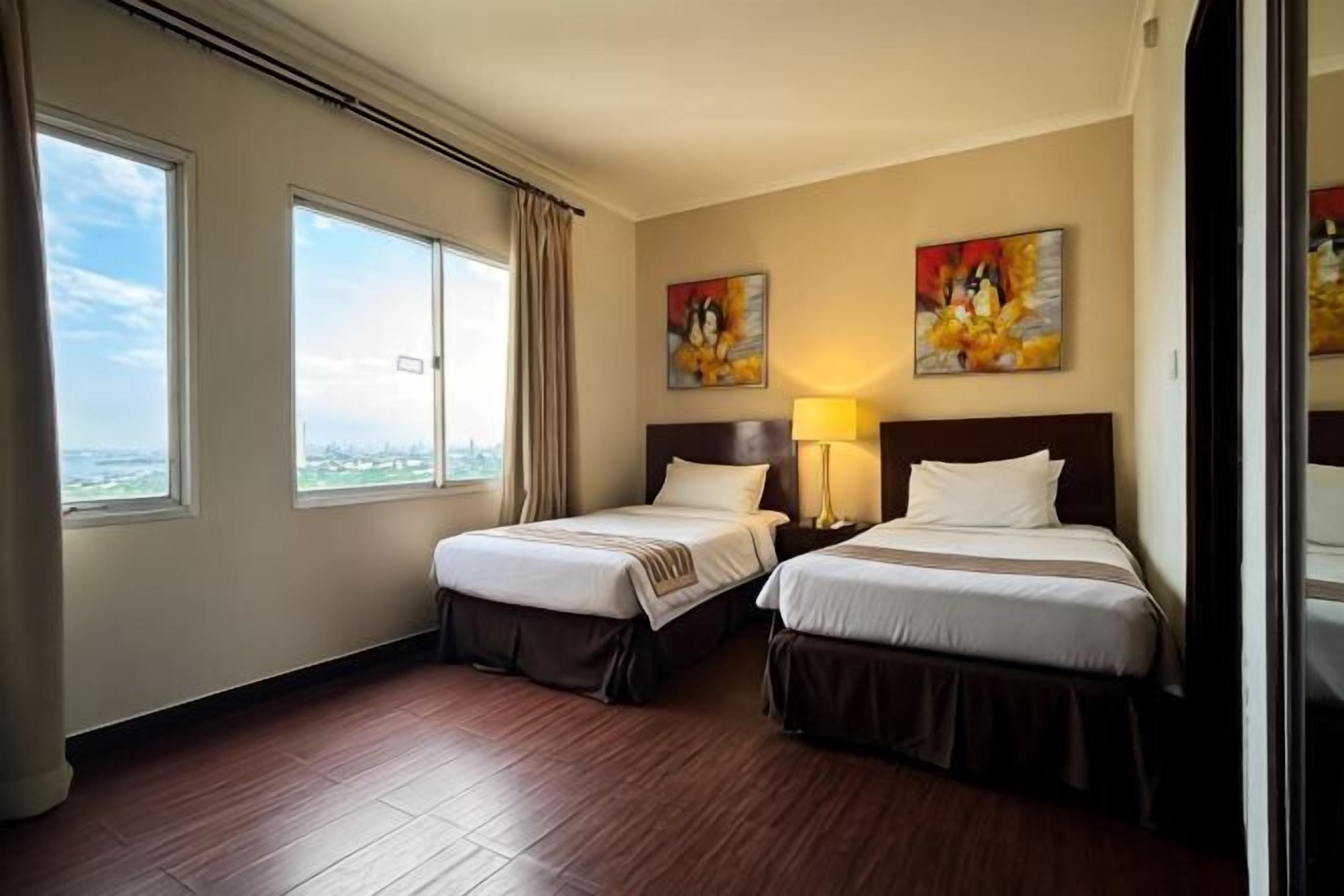 Une chambre d’hôtel avec deux lits, une grande fenêtre et des œuvres d’art accrochées aux murs.