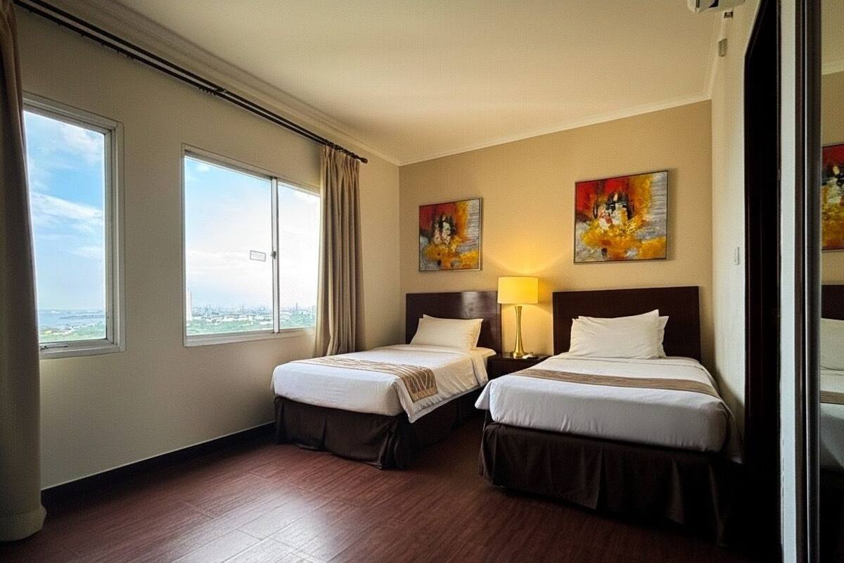 Une chambre d’hôtel avec deux lits, une grande fenêtre donnant sur un beau paysage et deux tableaux accrochés au mur.