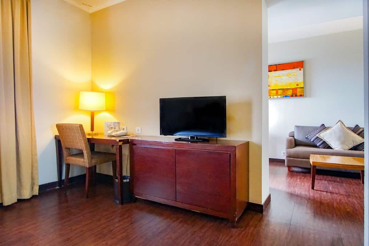 Une chambre d’hôtel avec un bureau en bois, une télévision, un canapé et un tableau au mur.