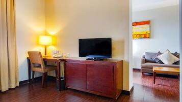 Habitación de hotel con un escritorio de madera, televisión, una silla, un sofá y un cuadro en la pared.
