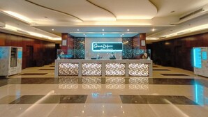 Uma área de recepção de hotel com design moderno, destacando um balcão de atendimento, painéis decorativos e uma grande placa iluminada.