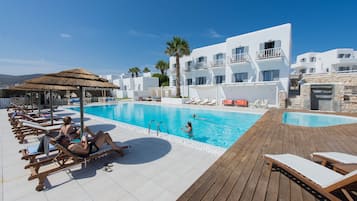 Relax by the pool surrounded by a wooden deck and stone wall, with comfortable sun loungers and a shaded cabana nearby.