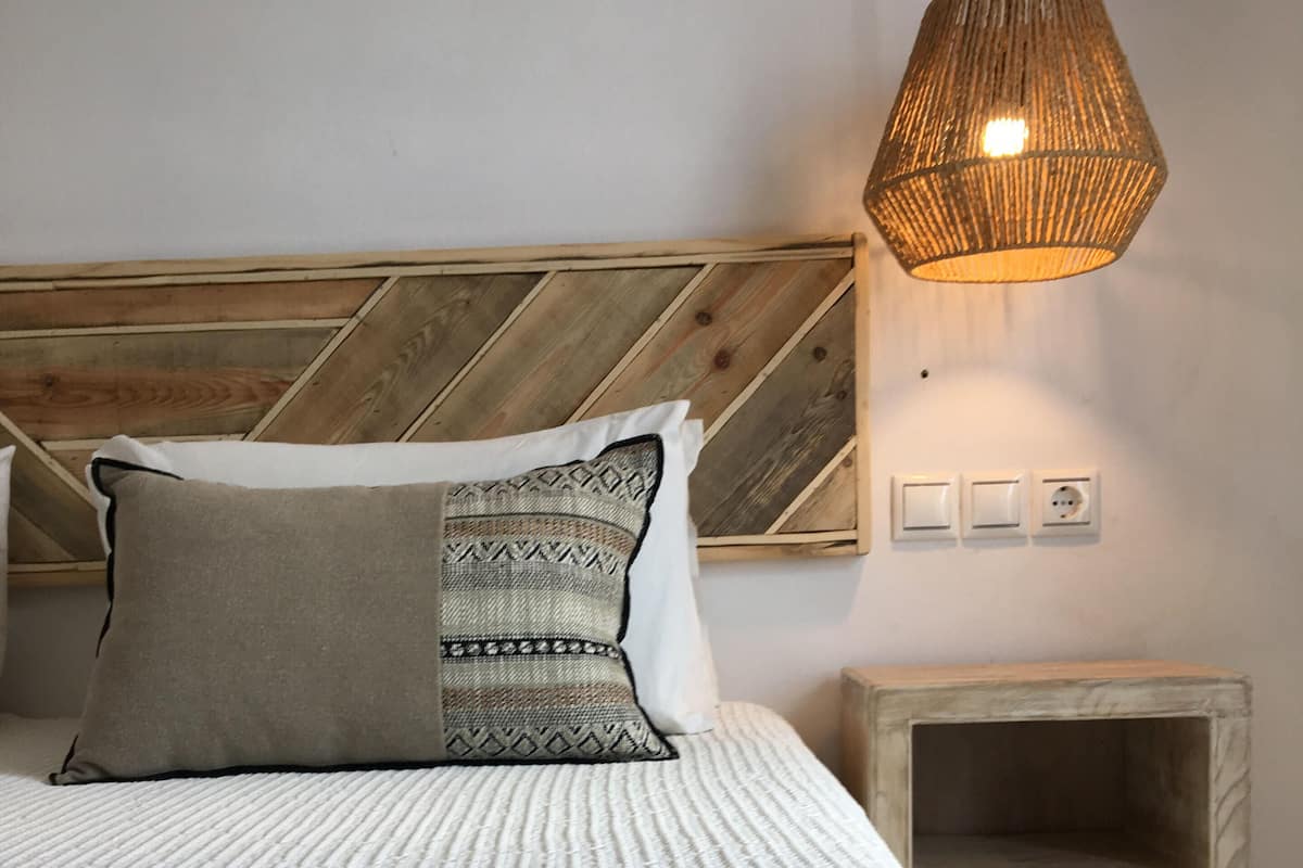 A neatly made bed with a patterned pillow, a wooden headboard, a bedside table, and a hanging light fixture.