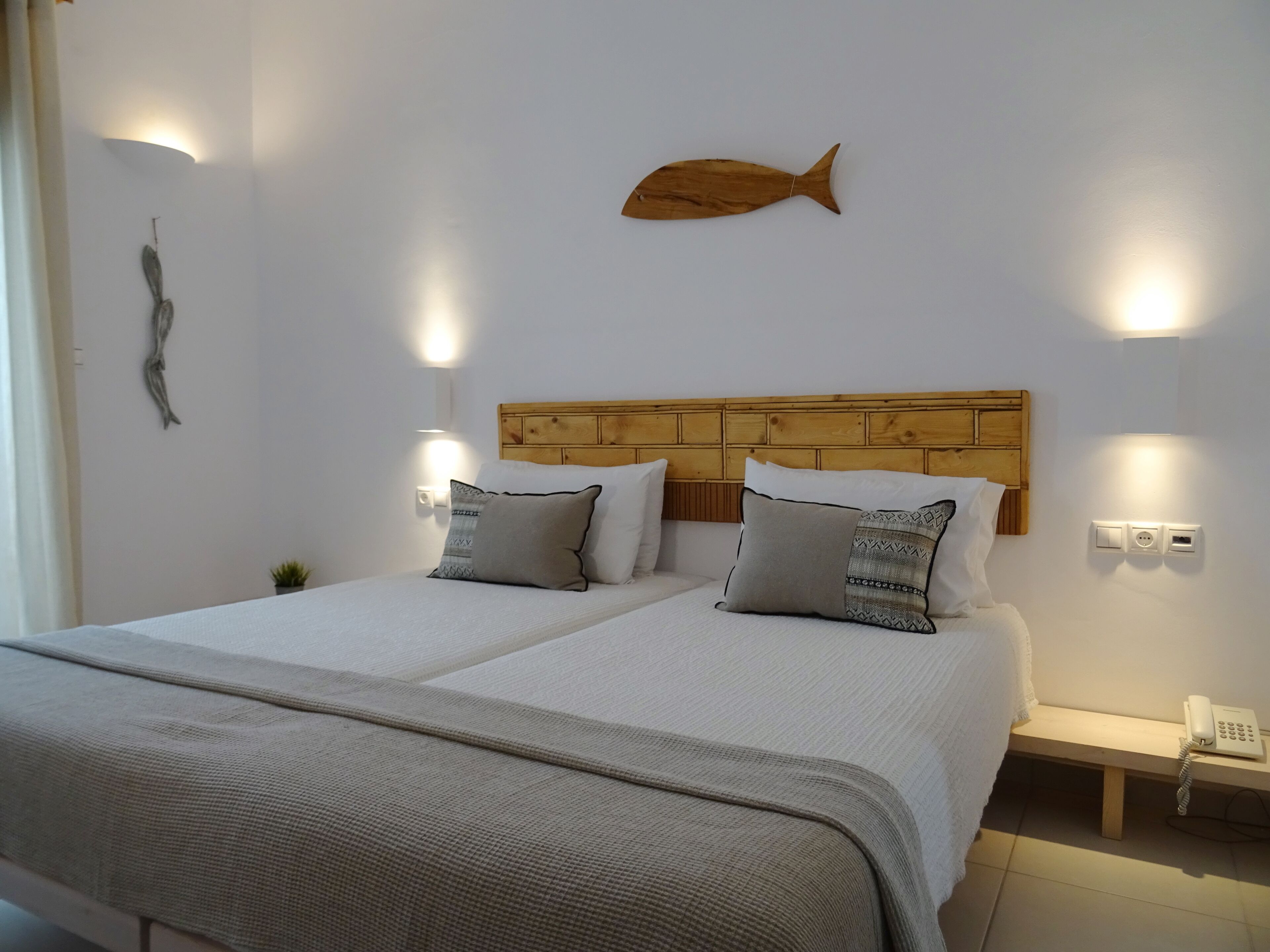 Een tweepersoonsbed met een houten hoofdeinde, twee nachtkastjes, een telefoon aan de muur en een decoratieve vis.