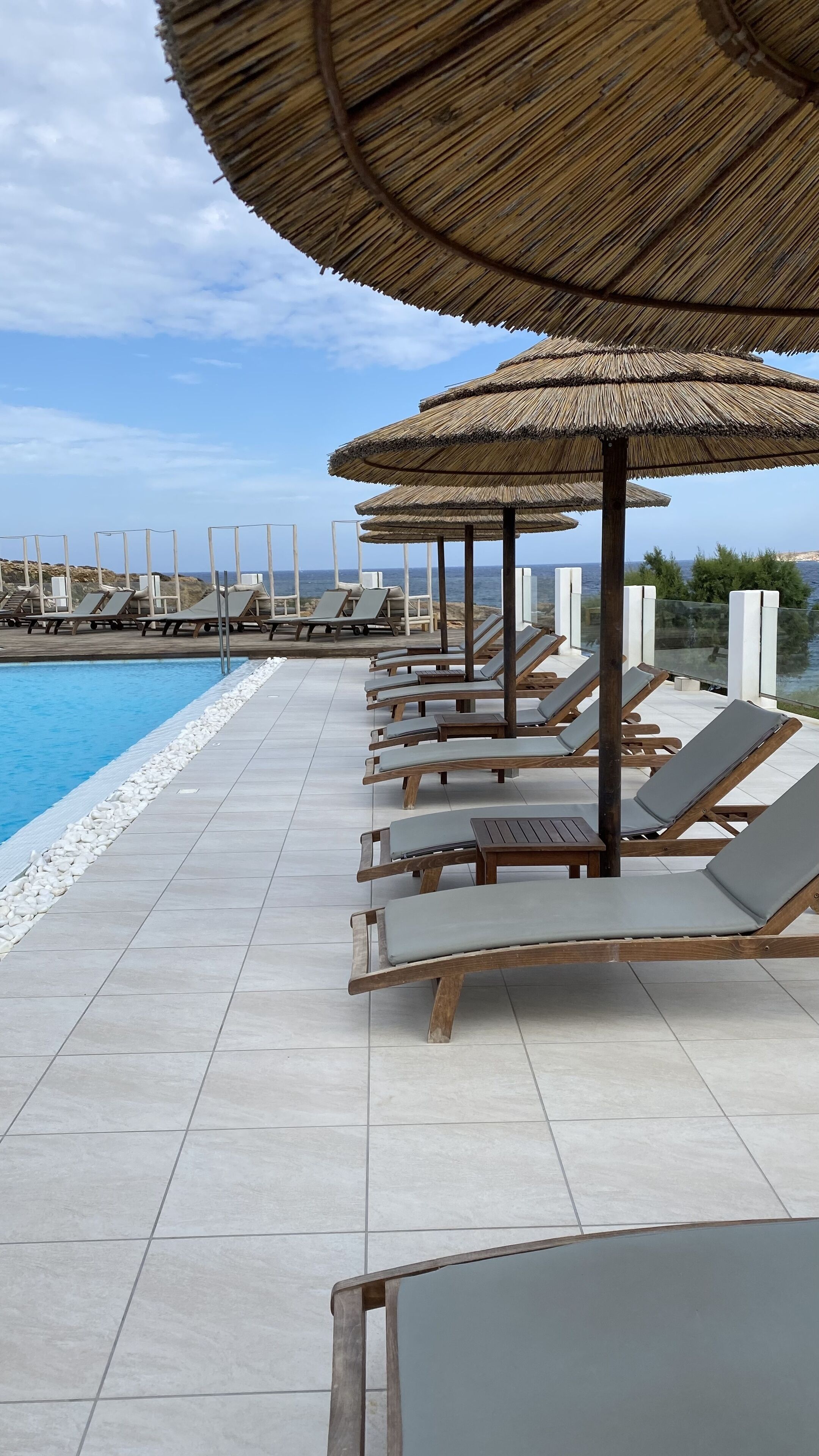 Zona de piscina con sillones de descanso y sombrillas de paja.