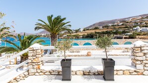 A coastal resort with stone walls, palm trees, and a pool area. - Paros Bay Hotel (Paros)