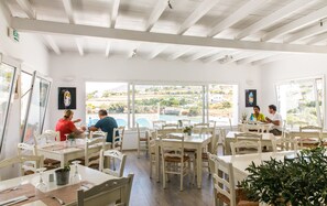 A bright dining area with white furniture, large windows offering views of the countryside, and an exit sign on the wall.