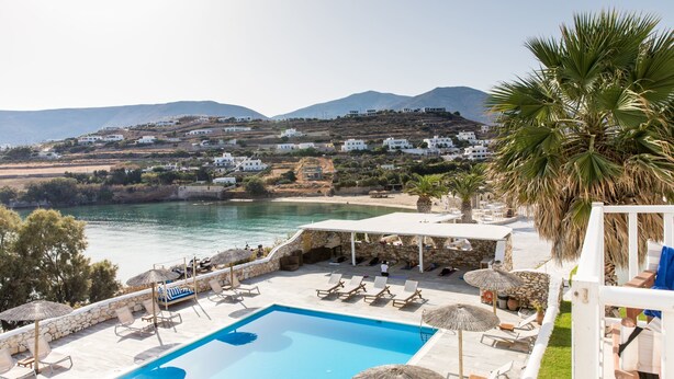 A pool area with lounge chairs and umbrellas, overlooking a beach and hills. - Paros Bay Hotel (Paros)