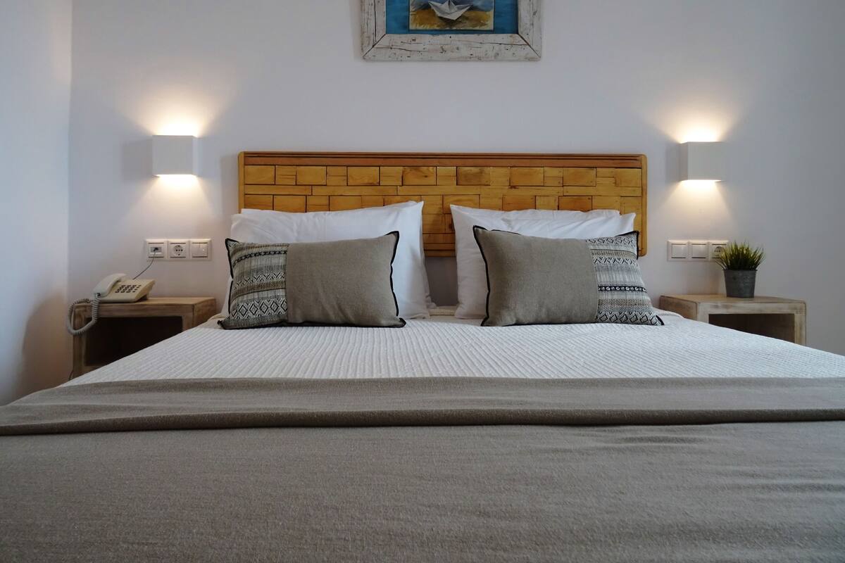 A neatly made bed with a wooden headboard, two bedside tables with lamps, and a painting above the headboard.