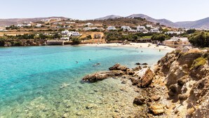 A coastal town with clear turquoise waters, rocky shoreline, and white buildings on a hillside. - Paros Bay Hotel (Paros)