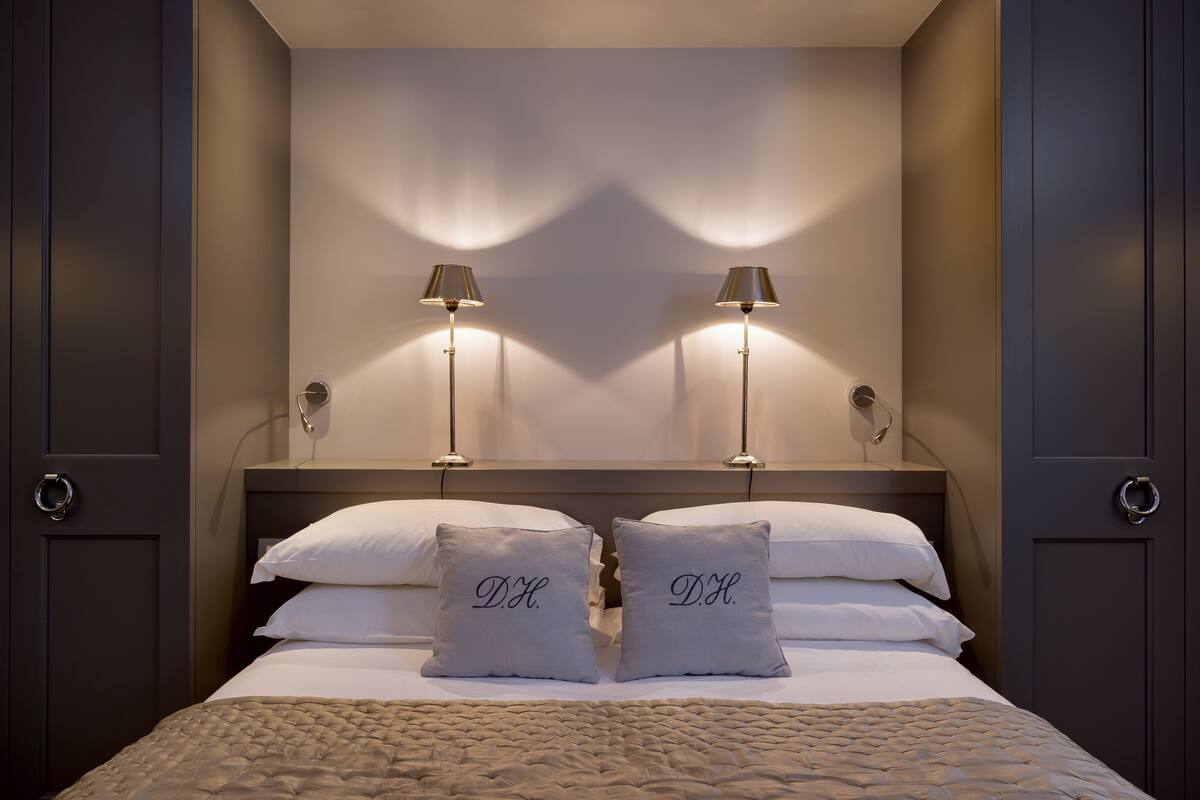 Un lit bien fait, avec deux oreillers, deux lampes de chevet et une tête de lit.