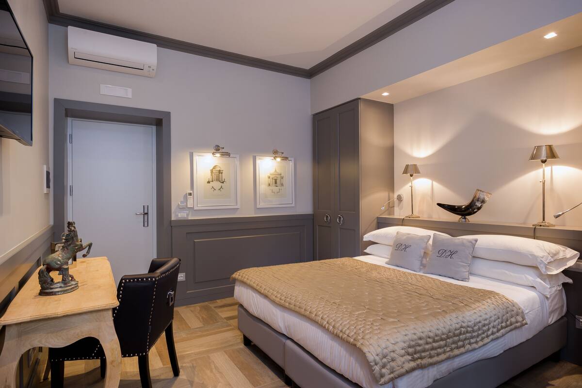 Une chambre à coucher comprenant un lit, des tables de chevet, un bureau et une chaise. On y trouve des lampes fixées au mur et un luminaire au plafond.