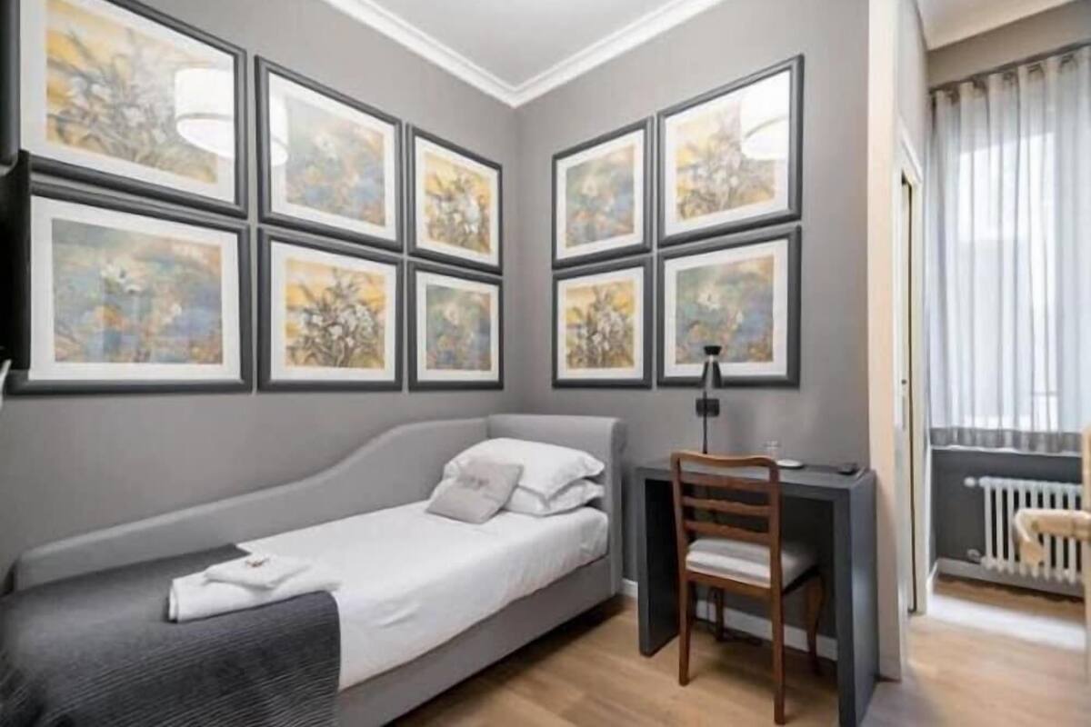 A bedroom with a bed, a desk, and a chair. There are six framed pictures on the wall.