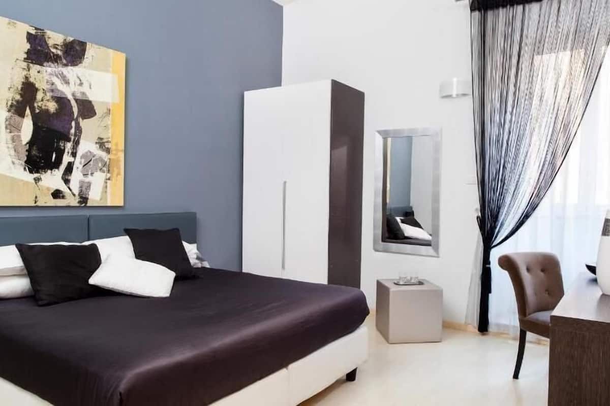 Une chambre d’hôtel comprenant un lit, une armoire, une télévision et un bureau agrémenté de deux vases.