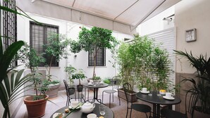 Un pati amb una taula rodona, cadires, plantes en testos i una petita zona de jardí.