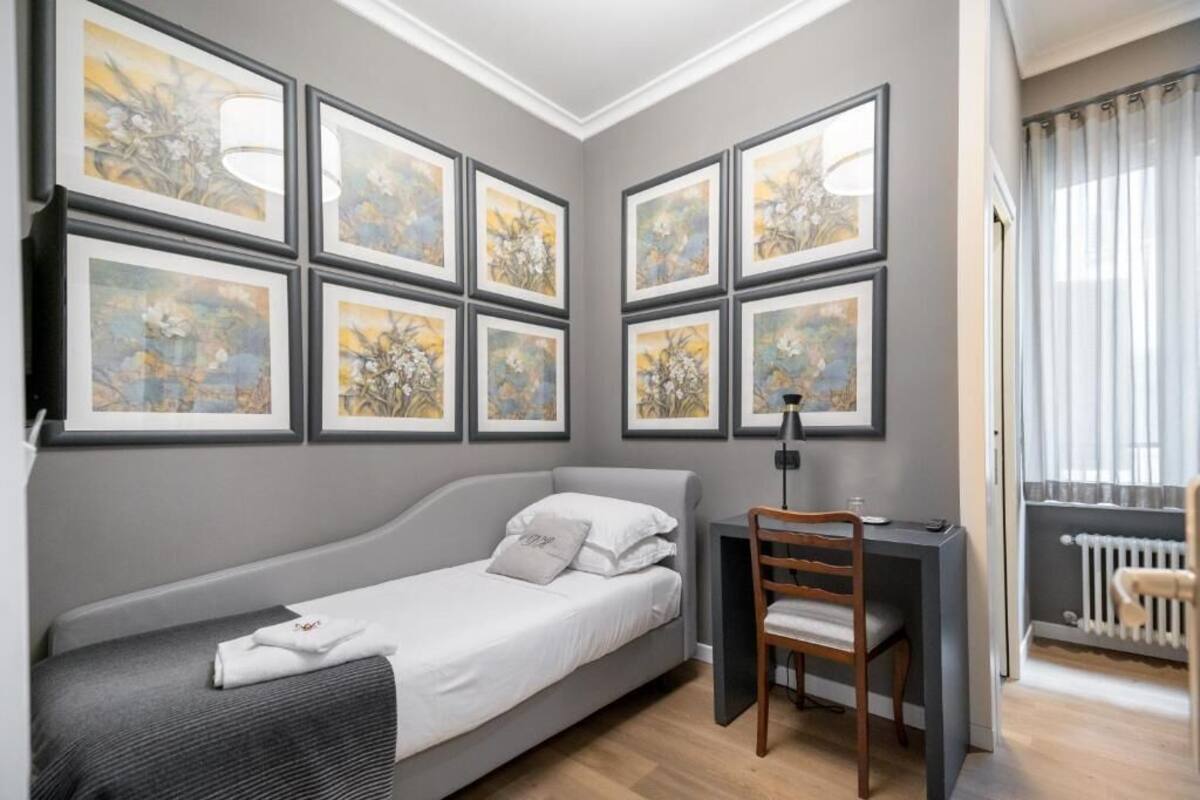 A compact room with a bed, a desk, and a chair. There are six framed artworks on the wall.