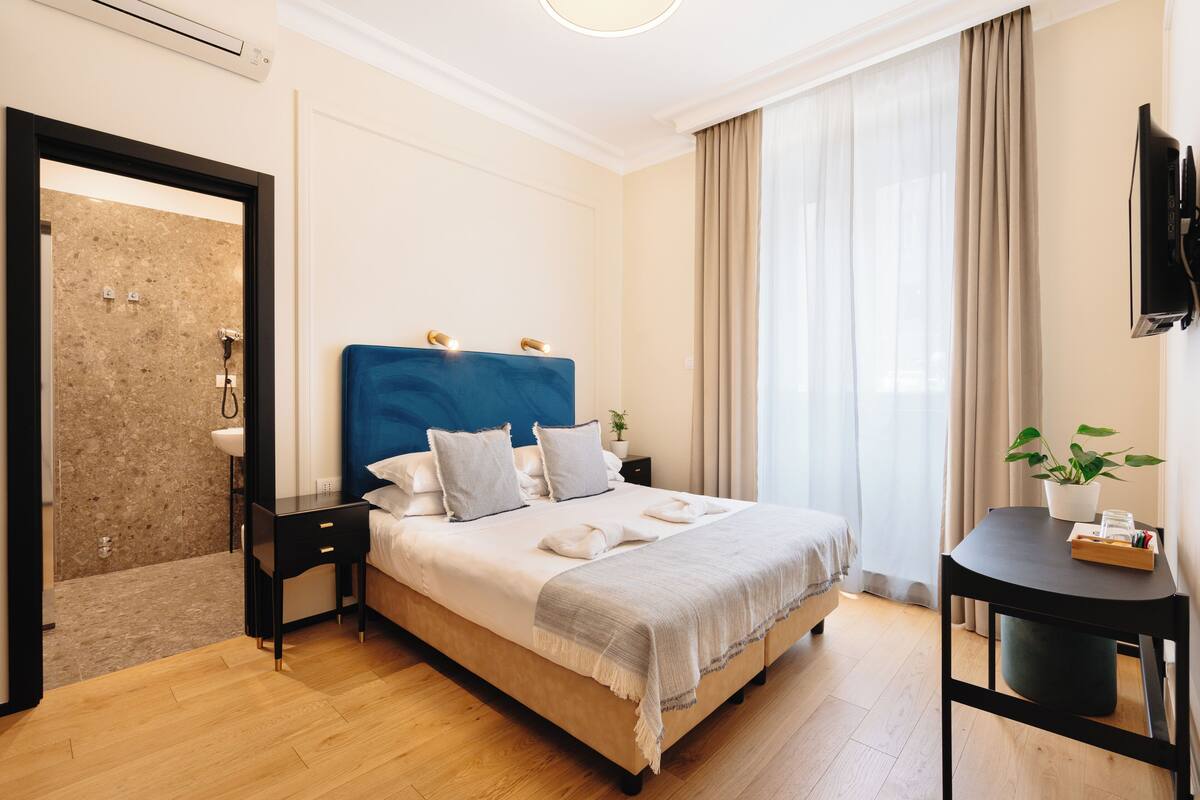 A modern hotel room with a large bed, a bedside table, a small desk, and a TV.