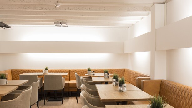A restaurant with booths and tables, wooden flooring, and potted plants on the tables. - Hotel Marktzicht (Harderwijk)