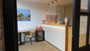 A reception area with a wooden counter, a small desk with a chair, a refrigerator stocked with beverages, and a wall-mounted key display. - Hotel Marktzicht (Harderwijk)