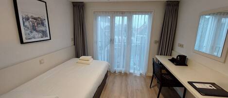 Habitación de hotel con cama, escritorio, silla, ventana con cortinas e imagen enmarcada en la pared.