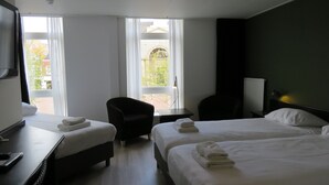 A hotel room with two beds, a desk, a chair, and a view of the outside. - Hotel Marktzicht (Harderwijk)