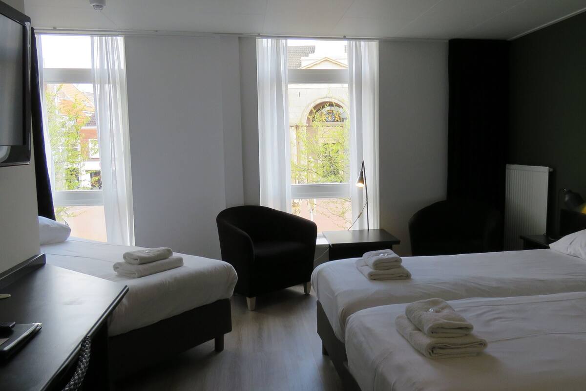 A hotel room with two beds, a desk, a chair, and a view of the outside.