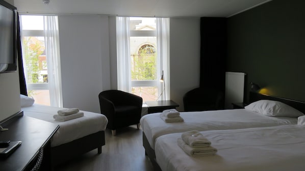 A hotel room with two beds, a desk, a chair, and a view of the outside.