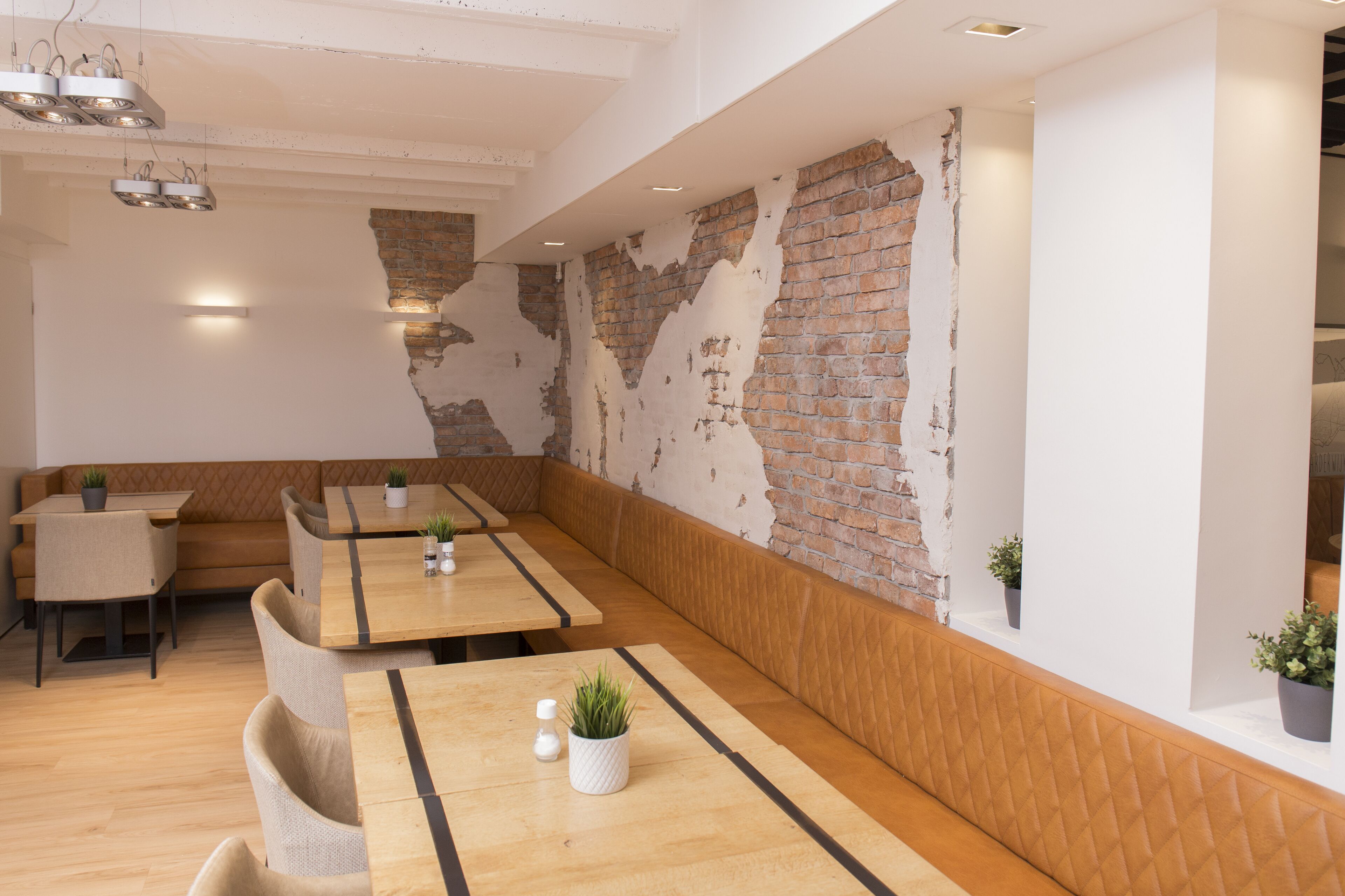 Ein modernes Restaurant mit Holztischen und -bänken, Ziegelwandelementen und Pendelleuchten.