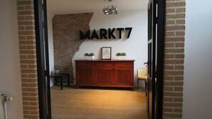 A hallway with a brick wall, a wooden cabinet with two potted plants, and a sign that reads "MARKT7". - Hotel Marktzicht (Harderwijk)