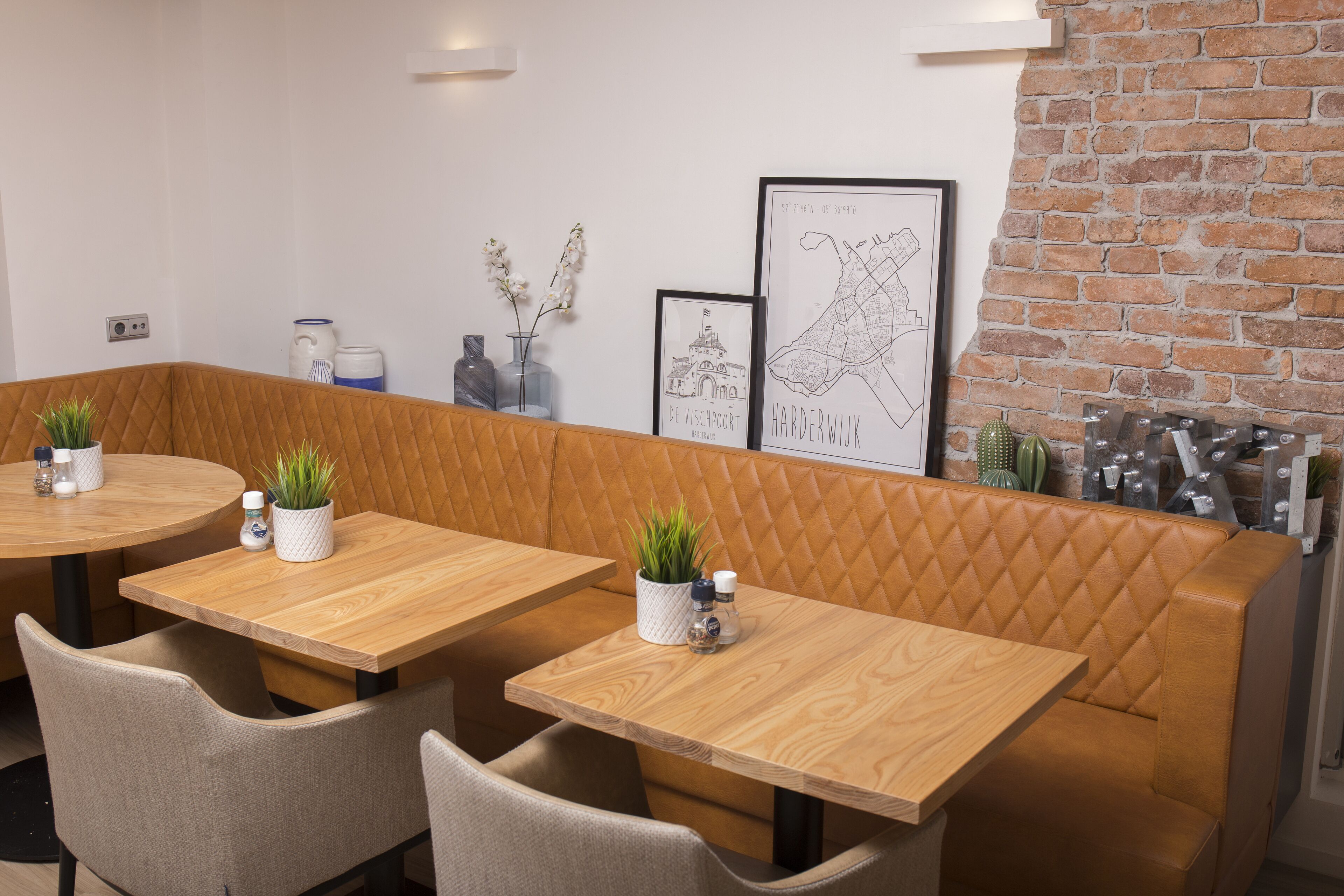A restaurant with wooden tables and cushioned booths, a brick wall, and framed artwork on the wall.