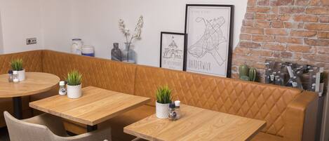 A restaurant with wooden tables and cushioned booths, a brick wall, and framed artwork on the wall.