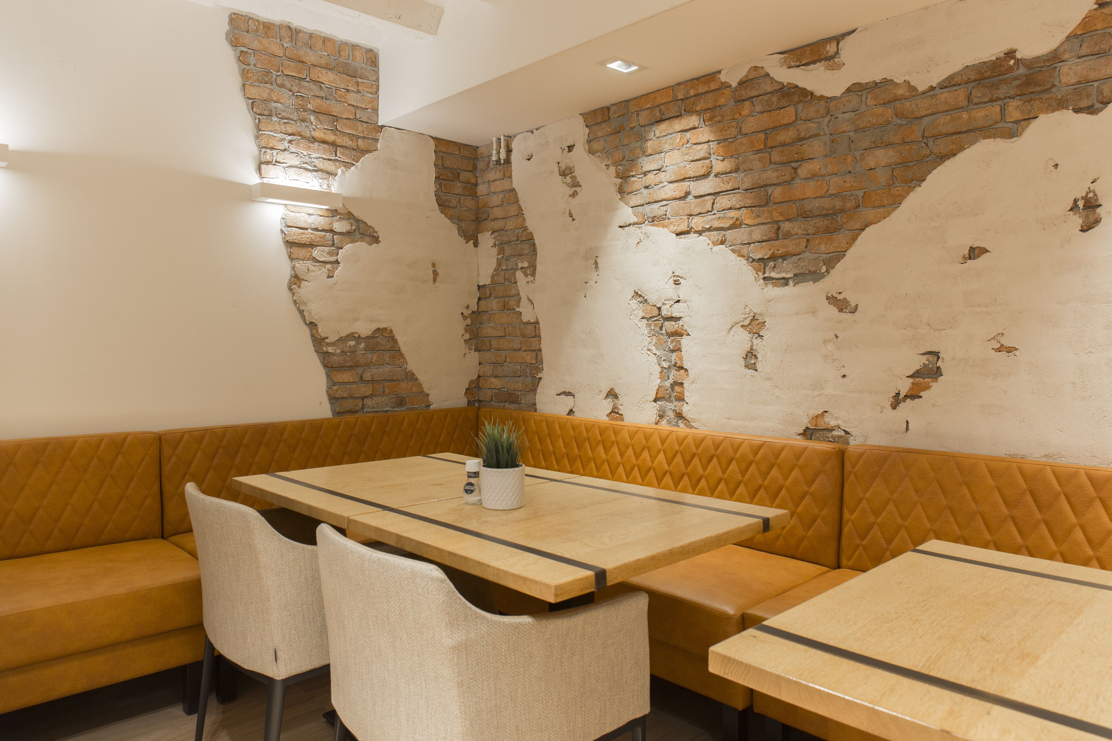 A restaurant interior with a brick wall, wooden tables, and cushioned seating.
