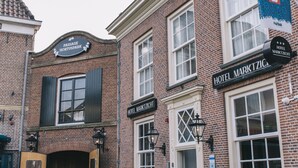 A brick building with signs for 'Passage Hortspark' and 'Hotel Marktzich'. There are outdoor tables and chairs, and a wooden door. - Hotel Marktzicht (Harderwijk)