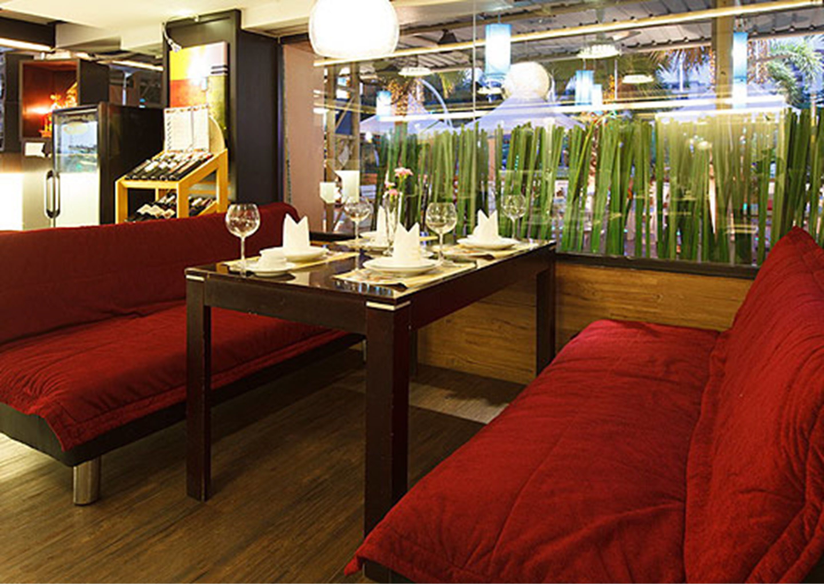 A restaurant with red upholstered seating, a wooden table, and a glass partition with plants.