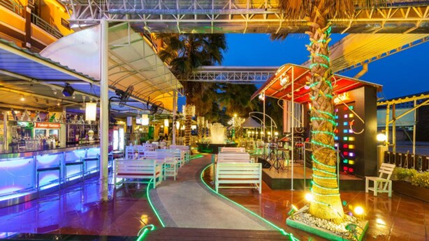 Een terras aan het water met buitenplaatsen, een palmboom en een overdekte doorgang.