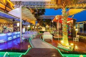 A waterfront bar area with outdoor seating, a palm tree, and a covered walkway. - Vabua Asotel Bangkok (Bangkok)