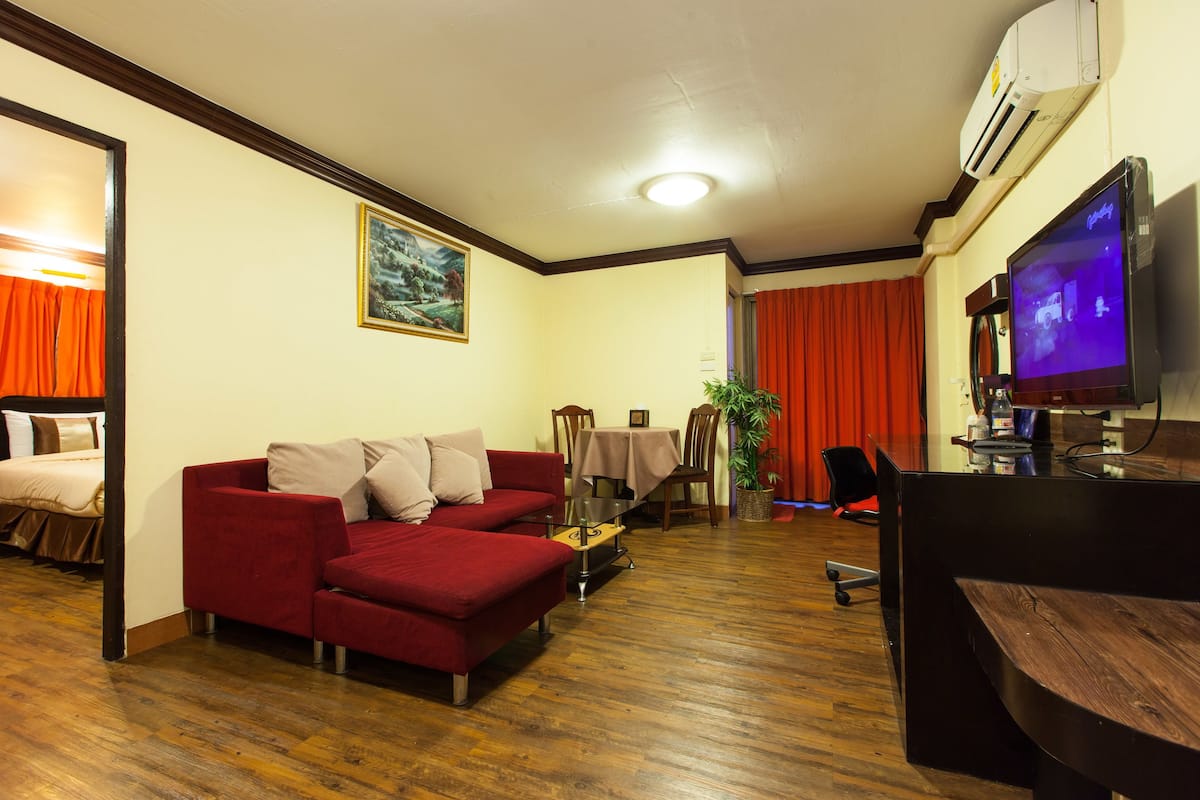 Ein Wohnzimmer mit einem roten Sofa, einem Holztisch, einem Fernseher und einem Essbereich mit Tisch und Stühlen.