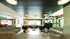 Een ruime lobby met een hoge plafond, verschillende zithoeken en een centrale salontafel.