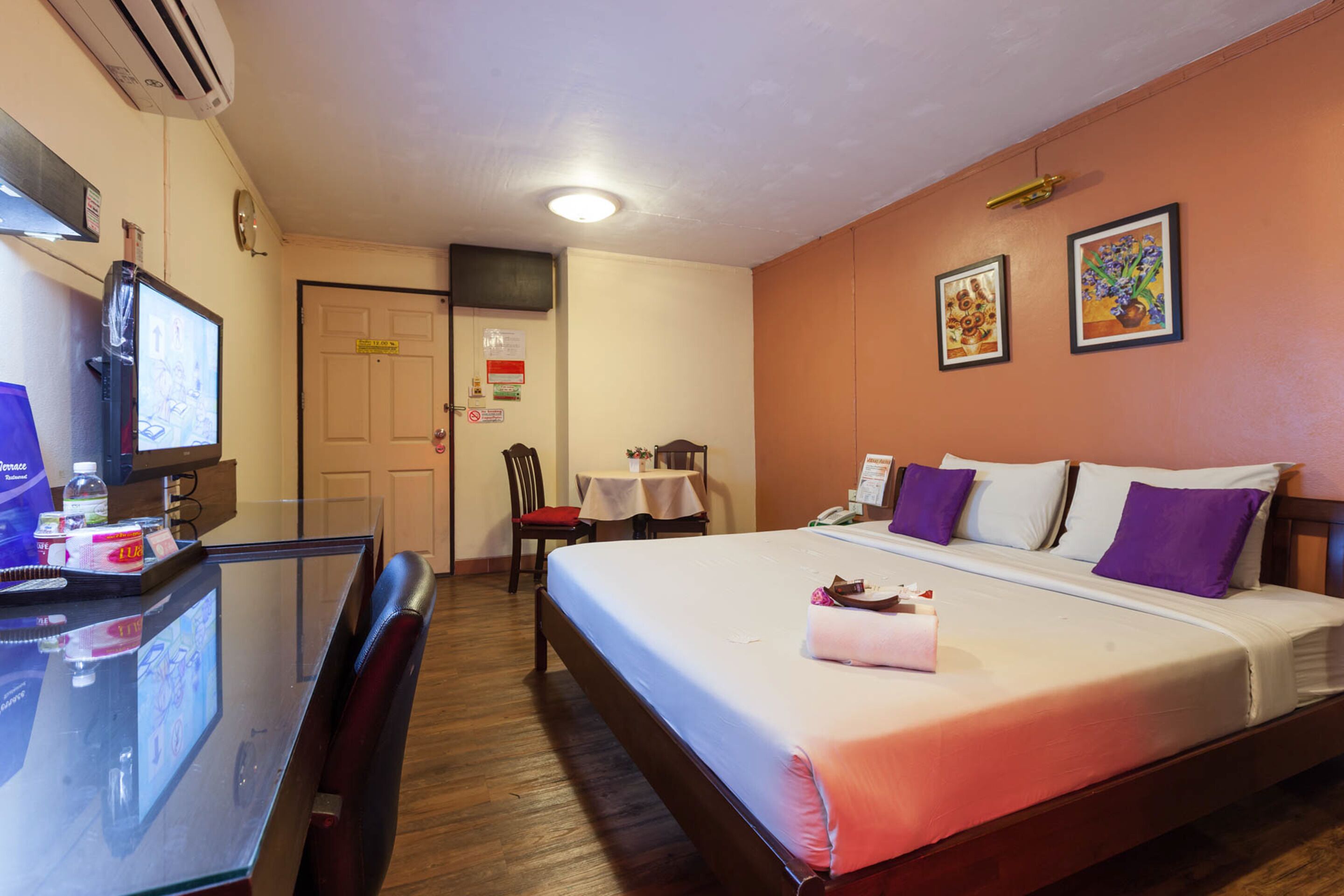 A hotel room with a bed, a desk with a computer, a chair, a table with a chair, and a door.
