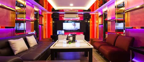A modern living room with a black leather sofa, a red sofa, and a coffee table. There is a flat-screen TV mounted on the wall, and a sound system with speakers.