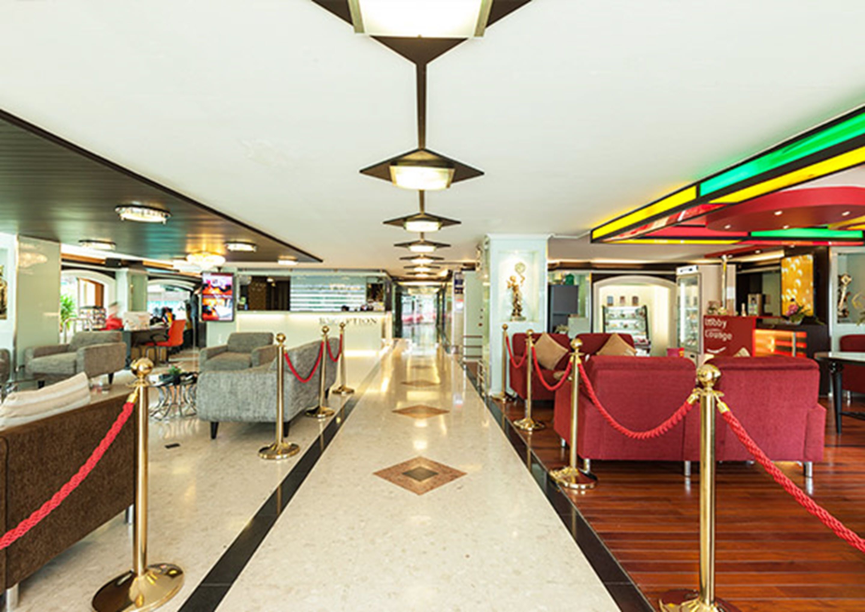 A hotel lobby with a central corridor, seating areas on both sides, and a reception desk.