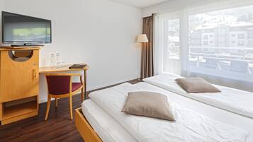 Een hotelkamer met een bed, een bureau met stoel, een televisie en een raam met uitzicht op gebouwen.