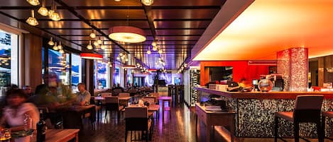 A restaurant with a long counter, multiple tables, and hanging pendant lights.