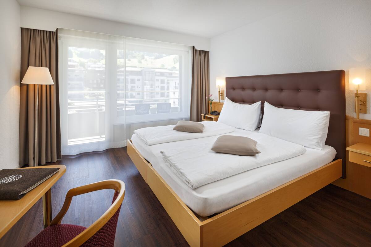 Een hotelkamer met een groot bed, een bureau, een stoel en een raam met gordijnen.