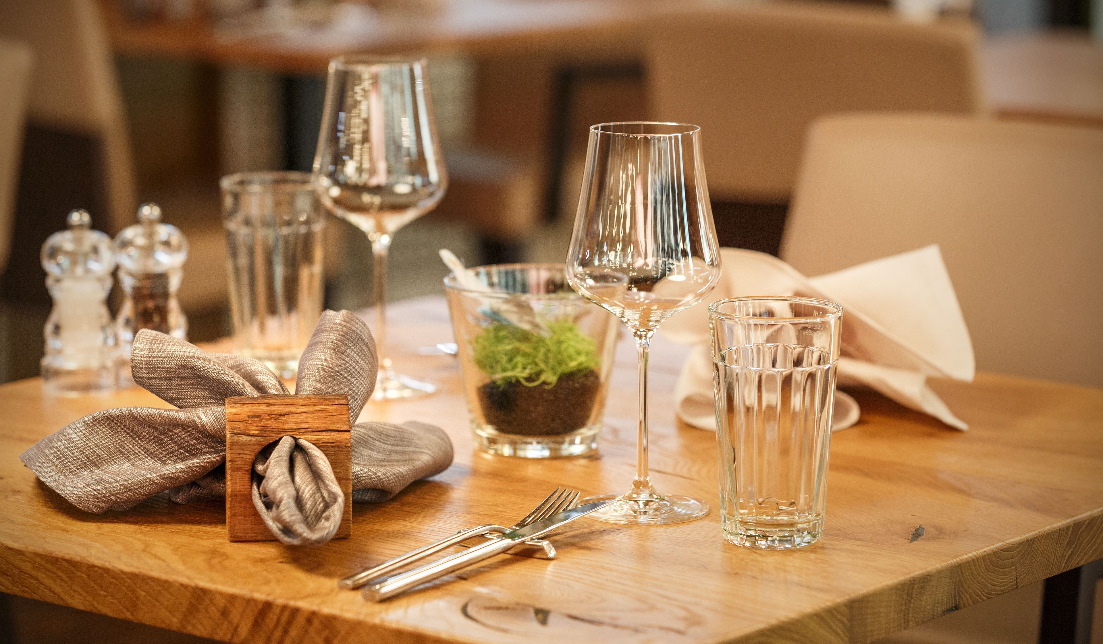 Et spisebord dækket med glas, en lille plante og en træ-napkinskål.