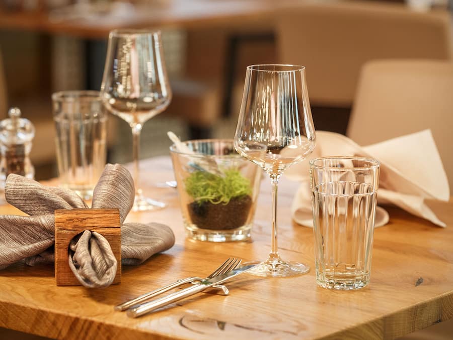 A dining table set with clear glassware, a small plant, and a wooden napkin holder.