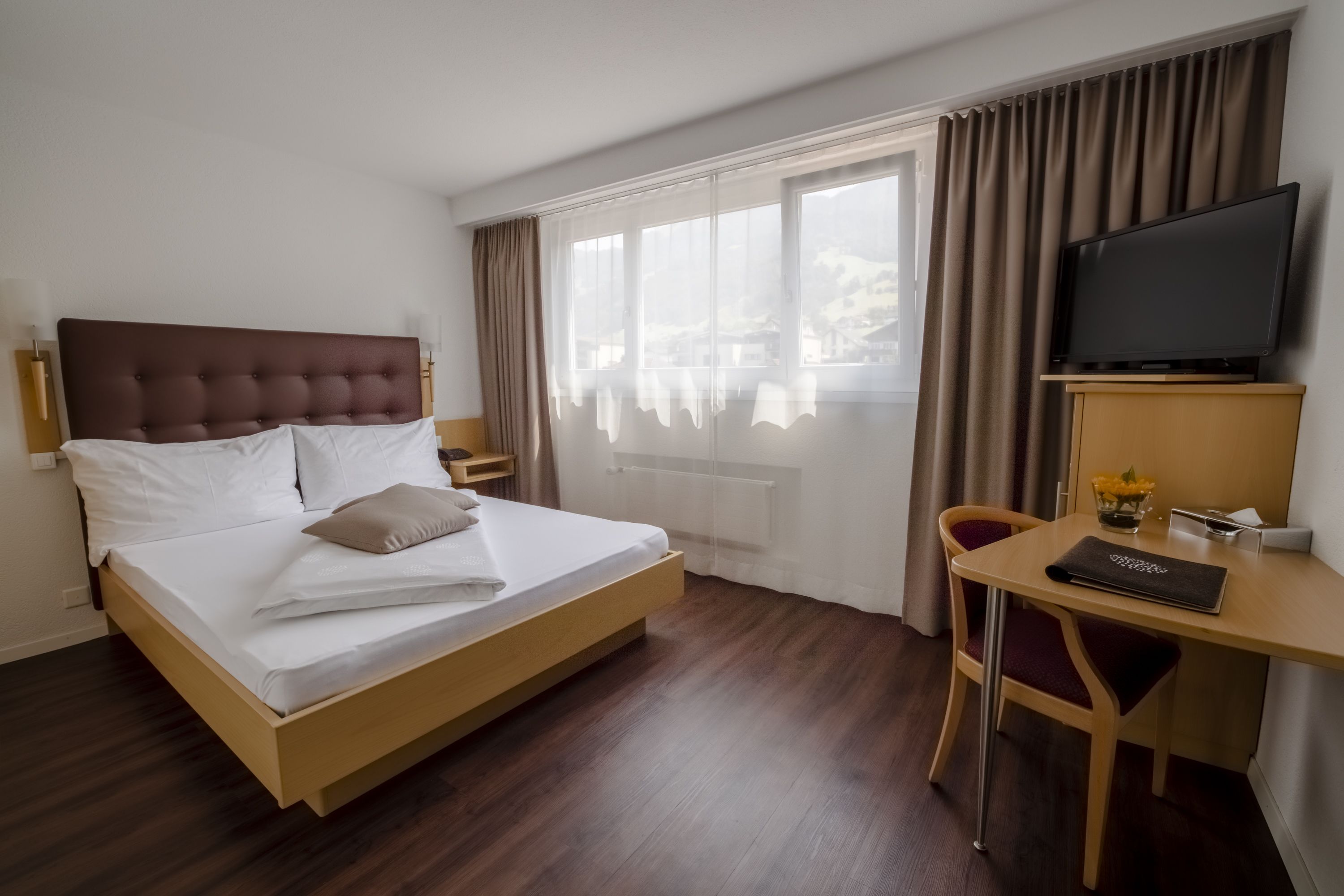 A hotel room with a bed, a desk, a chair, a television, and a window with curtains.