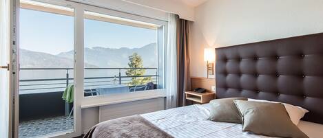 A hotel room with a large bed, a nightstand, a lamp, and a view of mountains through a sliding door.