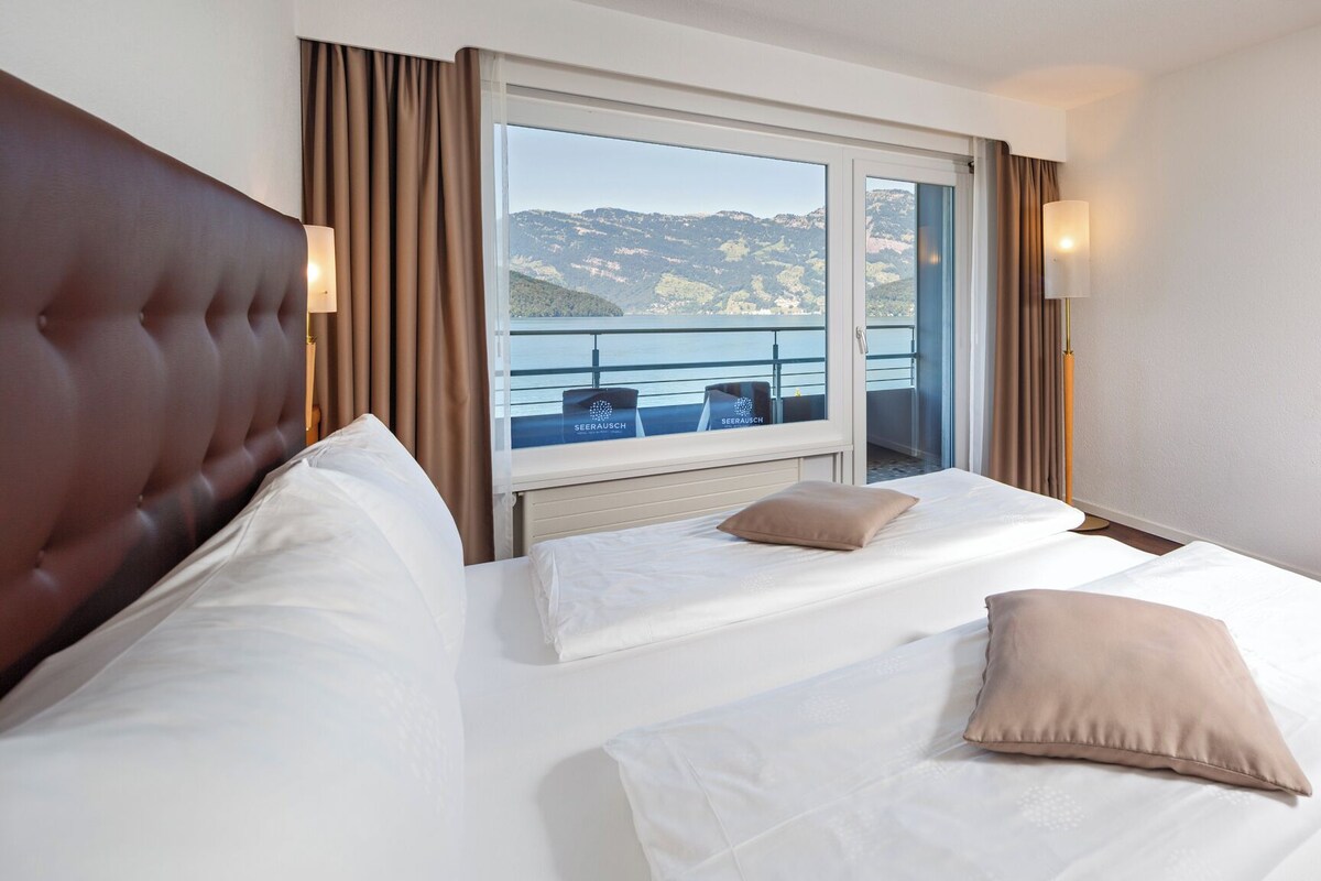 Habitación de hotel con una cama grande, vistas al mar y un balcón con mobiliario.