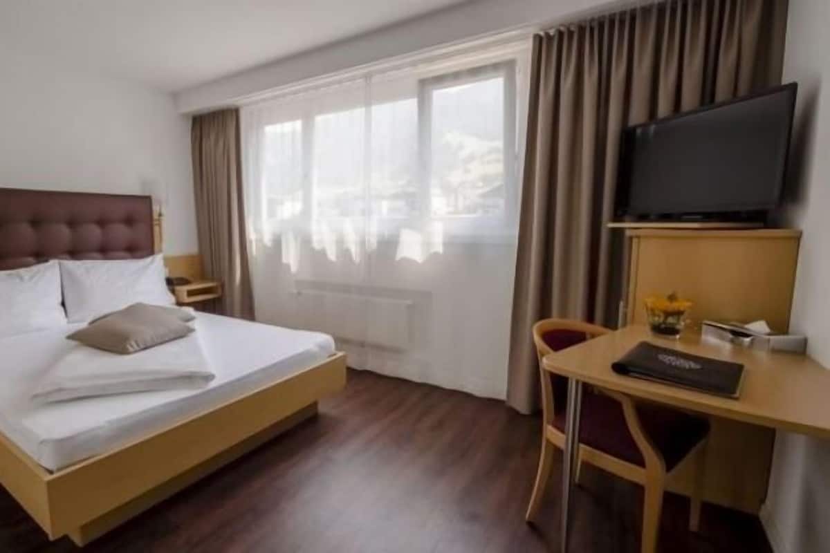 Een hotelkamer met een bed, een bureau, een stoel, een televisie en een raam met gordijnen.